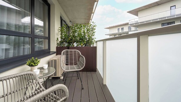 A balcony with wicker chairs, a small table, a potted plant, and a window. - Modern Apartment | Air Conditioning | Spa and Gym | Parking. (Wrocław)