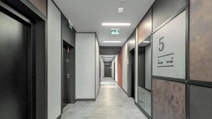 Un couloir moderne avec un sol carrelé, des portes numérotées et des panneaux indiquant les sorties de secours.