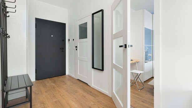Un couloir avec une porte sombre, un porte-manteau et une petite table.