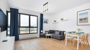 Un salon moderne comprenant un canapé, une table à manger et des chaises, de grandes fenêtres avec des rideaux et une vue sur la ville.