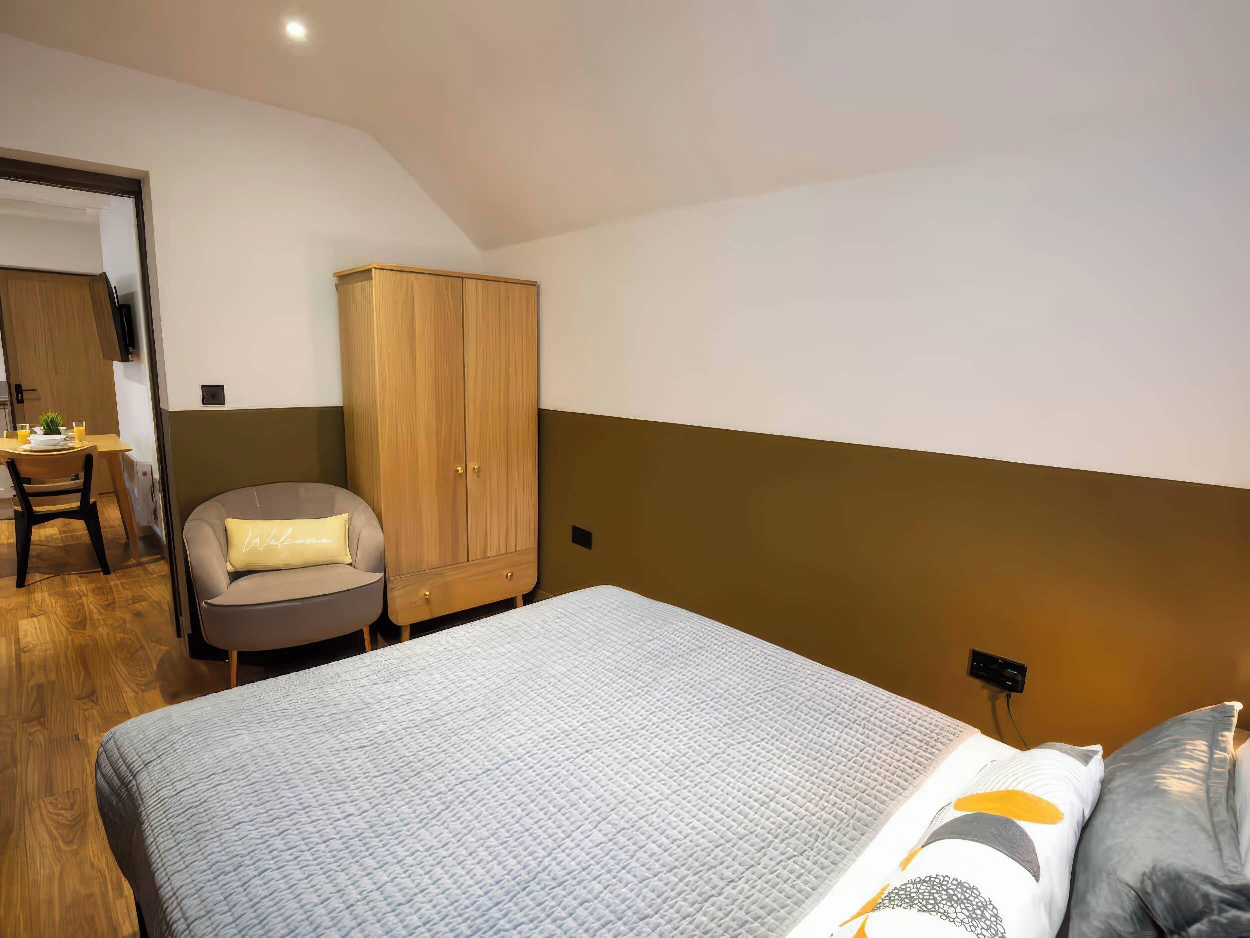 Ein Schlafzimmer mit einem Bett, einem Holzschrank, einem Stuhl und einem kleinen Tisch mit einer Pflanze.