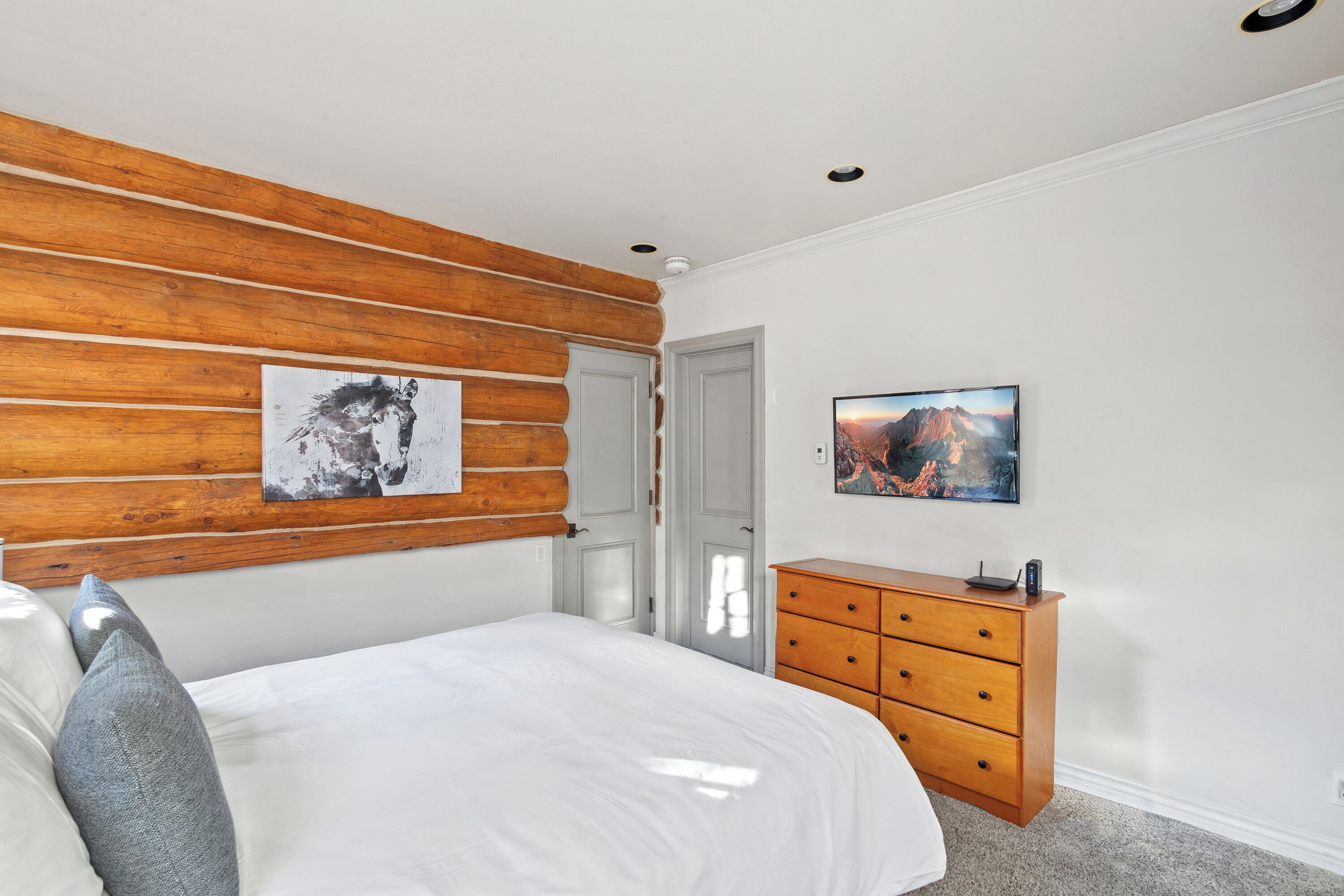 A bedroom with a wooden headboard, a bed with white bedding, a wooden dresser, and two framed pictures on the wall.