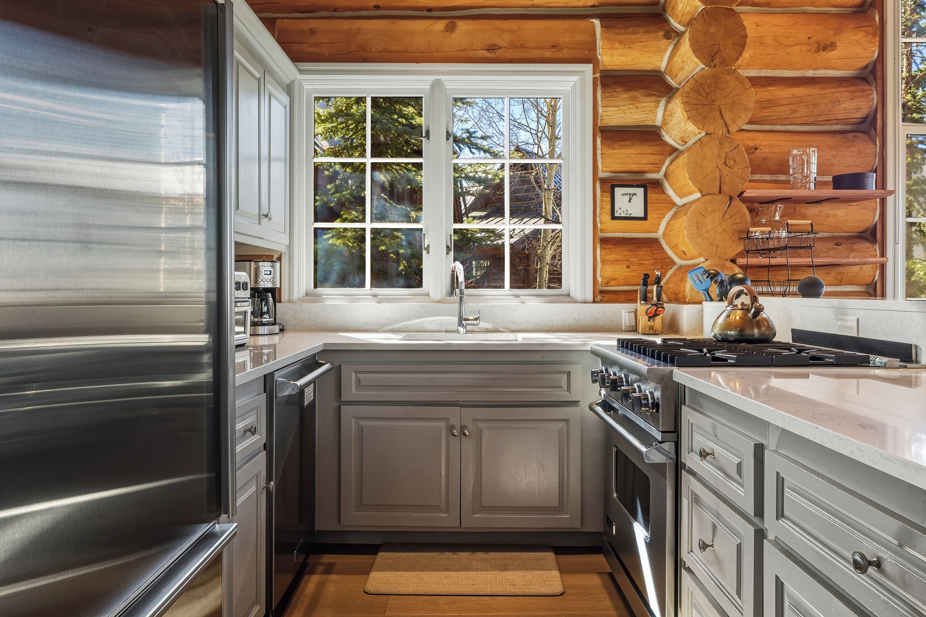 Una cocina moderna con un refrigerador de acero inoxidable, un lavamanos doble y un ventanal con vistas a árboles.