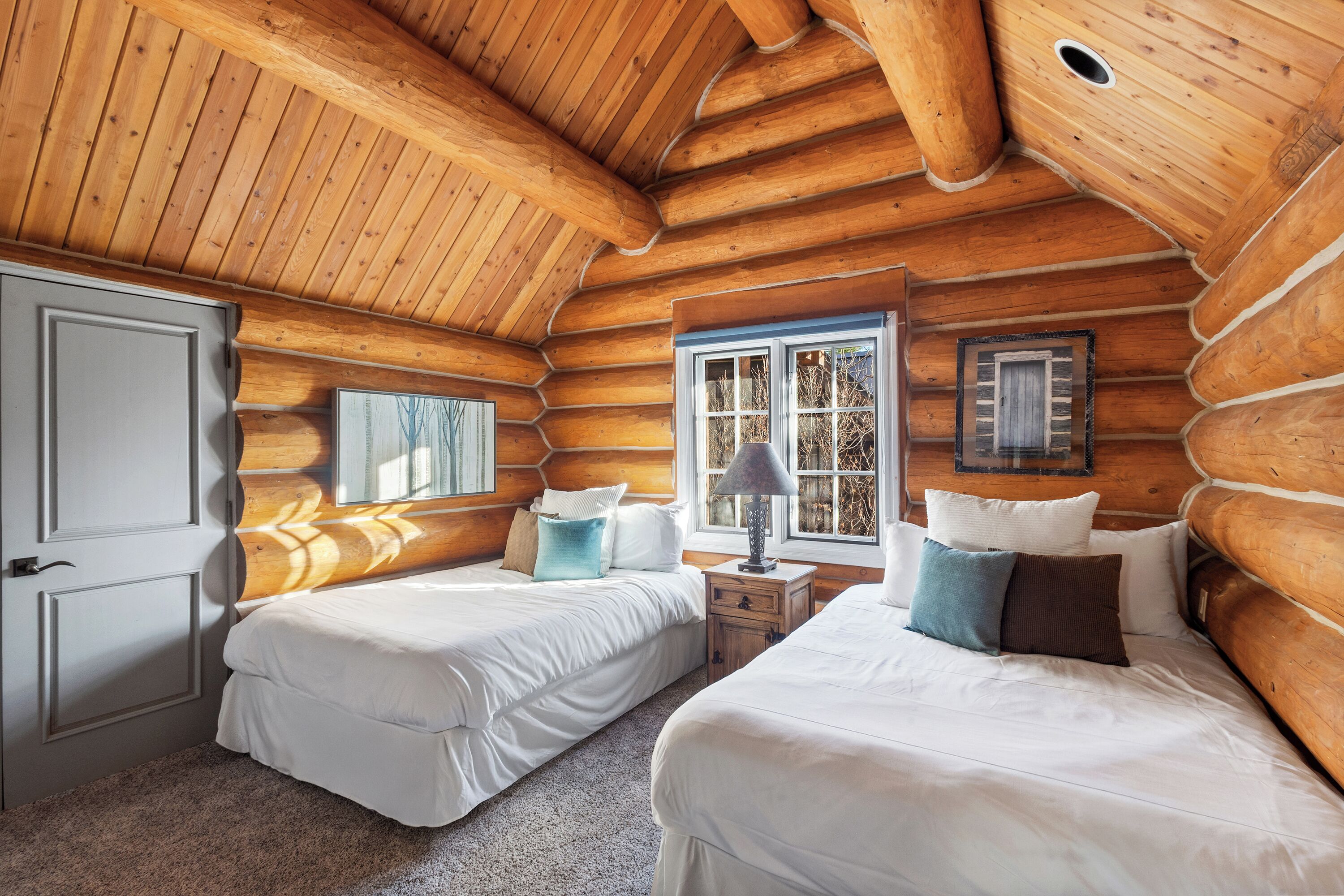 Ein Schlafzimmer in einer Blockhütte mit zwei Betten, einem Fenster und einer Tür.