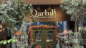 Uma área de estar externa com mesas e cadeiras, um tapete decorativo e uma placa com a inscrição 'Qartuli Authentic Georgian'.