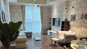 Uma sala de estar moderna com piso de madeira, uma área de refeições com mesa posta para quatro pessoas e uma grande planta em vaso.