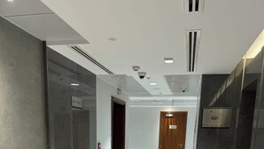 Um corredor com piso de mármore, uma porta de madeira no final e uma placa na parede.