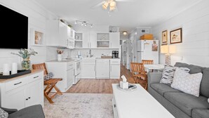 A modern kitchen with white cabinetry, a dining area with a grey sofa, and a ceiling fan. - Salty Smiles (Hilton Head Island)