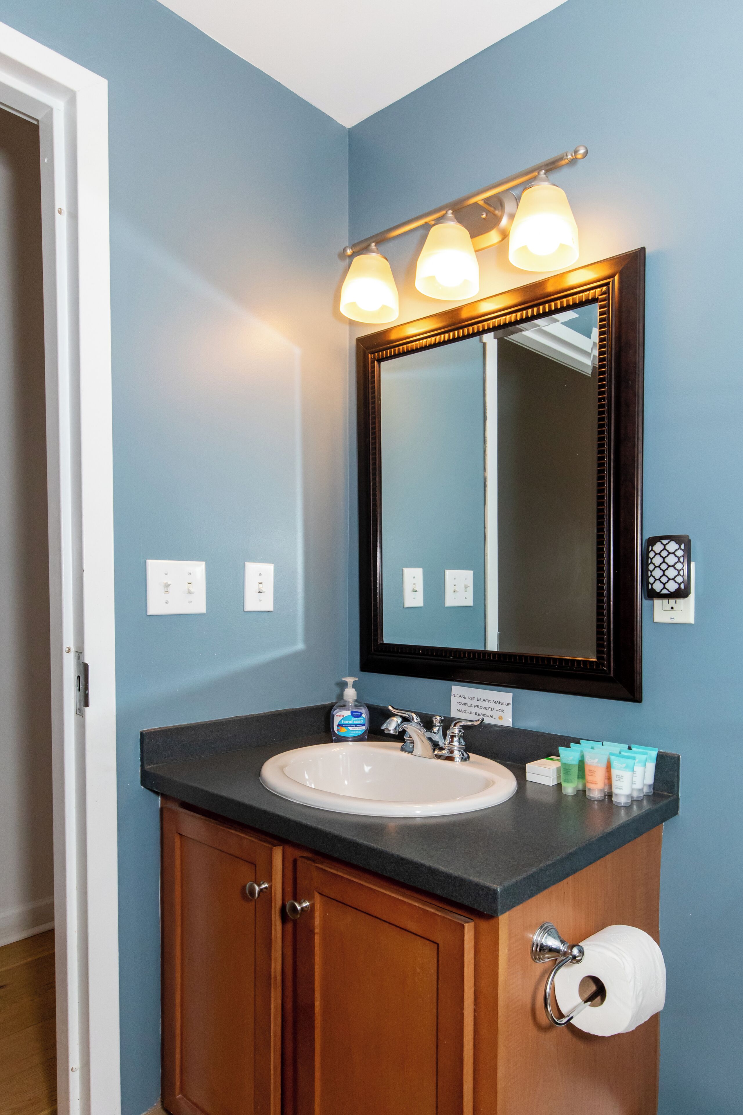 A bathroom with a white sink, a mirror with lights, and toiletries on the counter.