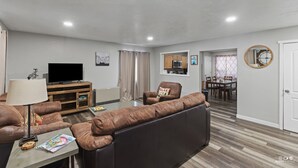 A living room with a sofa, TV, and a dining area with a table and chairs. - Bighorn Cabin - Entire cabin (Soldotna)
