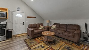 A living room with two brown leather sofas, a wooden coffee table, a patterned rug, a microwave, a trash bin, and a door with a sign. - Bighorn Cabin - Entire cabin (Soldotna)