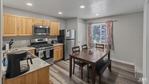 A modern kitchen with wooden cabinets, stainless steel appliances, and a dining area with a table and chairs. - Bighorn Cabin - Entire cabin (Soldotna)