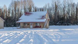 A two-story house with a snow-covered roof and a porch with red chairs. - Bighorn Cabin - Entire cabin (Soldotna)