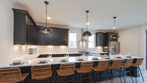 A modern kitchen with dark cabinetry, a central island with bar seating, and pendant lighting. - ♨️🌃 Hot Tub Heaven A, B, C&D @ The Gulch (Nashville)