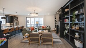 A modern kitchen with a dining area, a living room with a sofa and chairs, and a bookshelf filled with decorative items. - ♨️🌃 Hot Tub Heaven A, B, C&D @ The Gulch (Nashville)