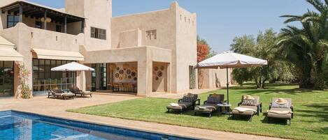 A modern house with a swimming pool, outdoor seating, and a well-maintained lawn.