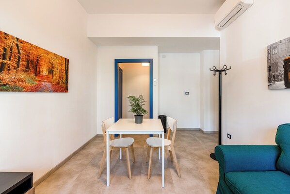 A small, well-lit room with a dining table and chairs, a green sofa, and a coat rack. - K-ROOMS - Central Station by InnStay (Milan)