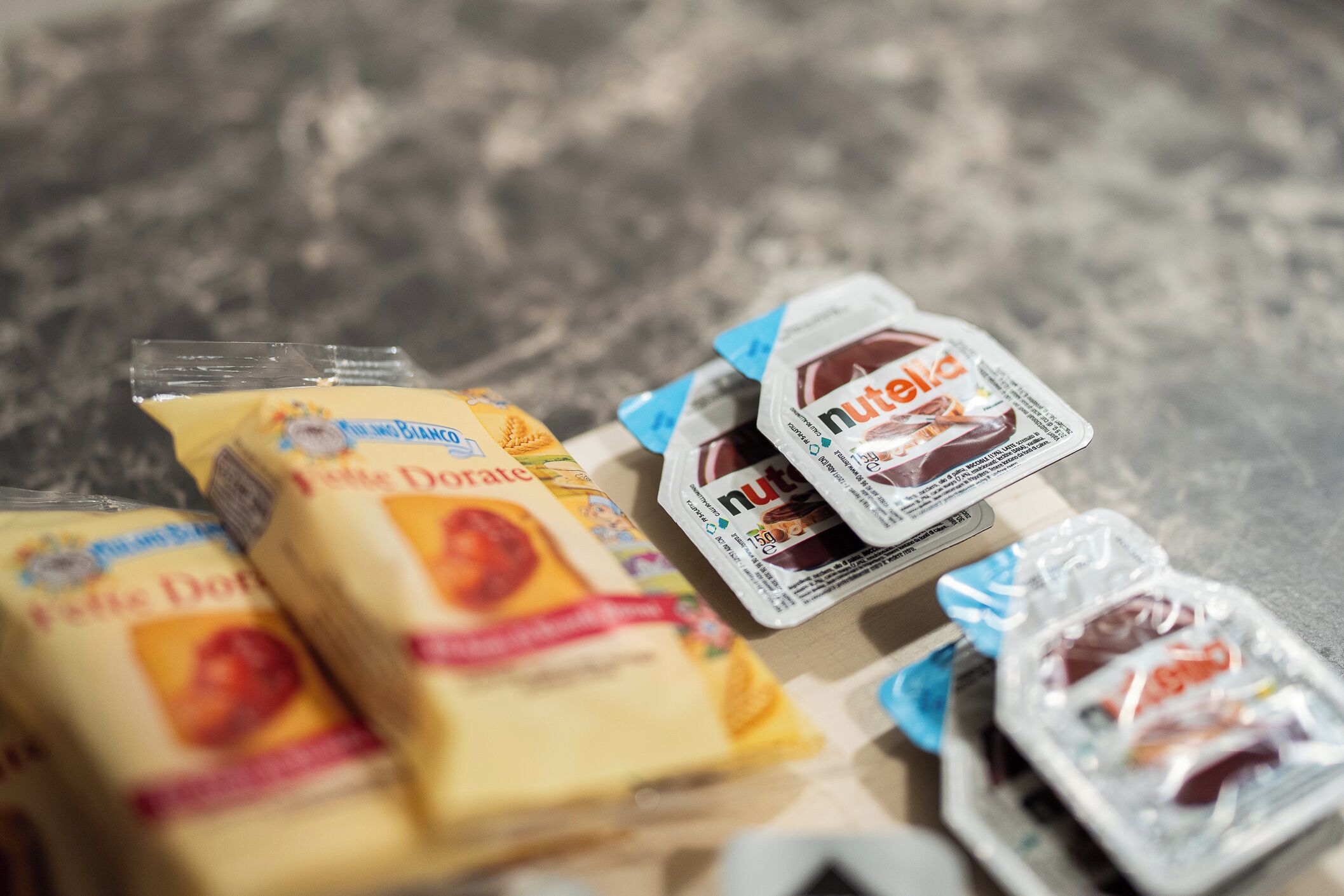 Diverse etenspakketten, waaronder 'Petit Doré' kaas en 'Nutella' spreads, op een oppervlak gerangschikt.