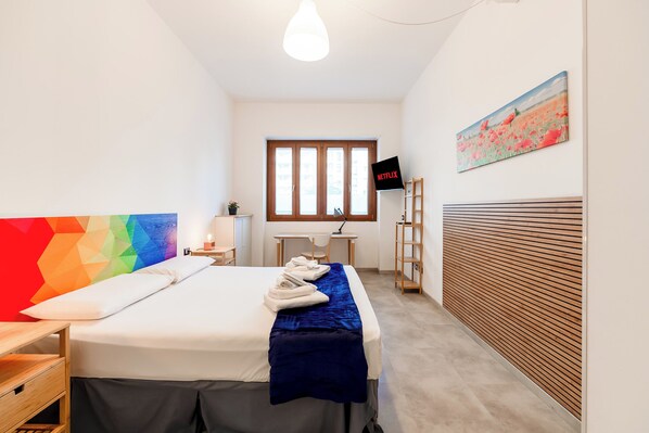Hotellihuone, jossa on sänky, työpöytä, tuoli, televisio ja taulu seinällä.