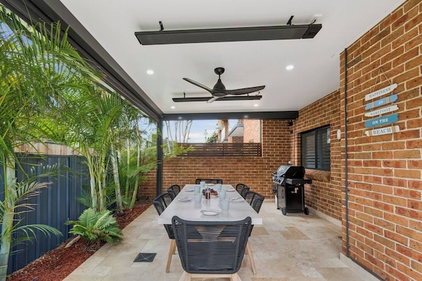 Dine alfresco beneath the covered patio, where a ceiling fan, gas BBQ, and lush tropical greenery create the perfect setting for leisurely summer evenings.
