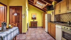 A kitchen with wooden cabinets, a tiled floor, a dining table with a plaid tablecloth, and a television mounted on the wall. - Rural Apartments La Viña (Apartment number 8) (Cangas de Onis)