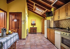 Eine Küche mit Holzausbau, Fliesenboden, einem Esstisch mit kariertem Tischläufer und einem an der Wand befestigten Fernseher.