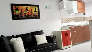 Un salon moderne avec un canapé noir, un meuble rouge et un coin cuisine doté de meubles blancs et d’un pare-feu en carrelage.