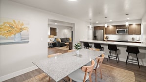 A modern kitchen with a central island, a dining area with a granite table, and a living room with a sofa and a painting. - Adventure Awaits at The Lake Loft (Coeur d`Alene)