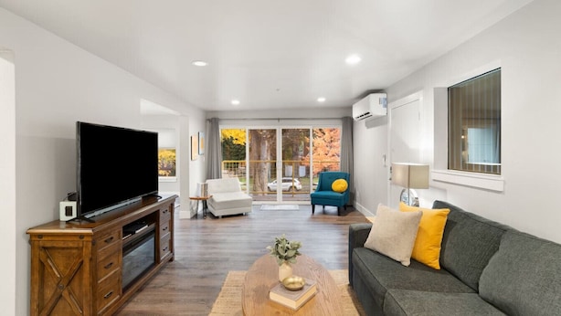 A modern living room with a flat-screen TV, wooden entertainment unit, grey sofa, and a coffee table. - Adventure Awaits at The Lake Loft (Coeur d`Alene)