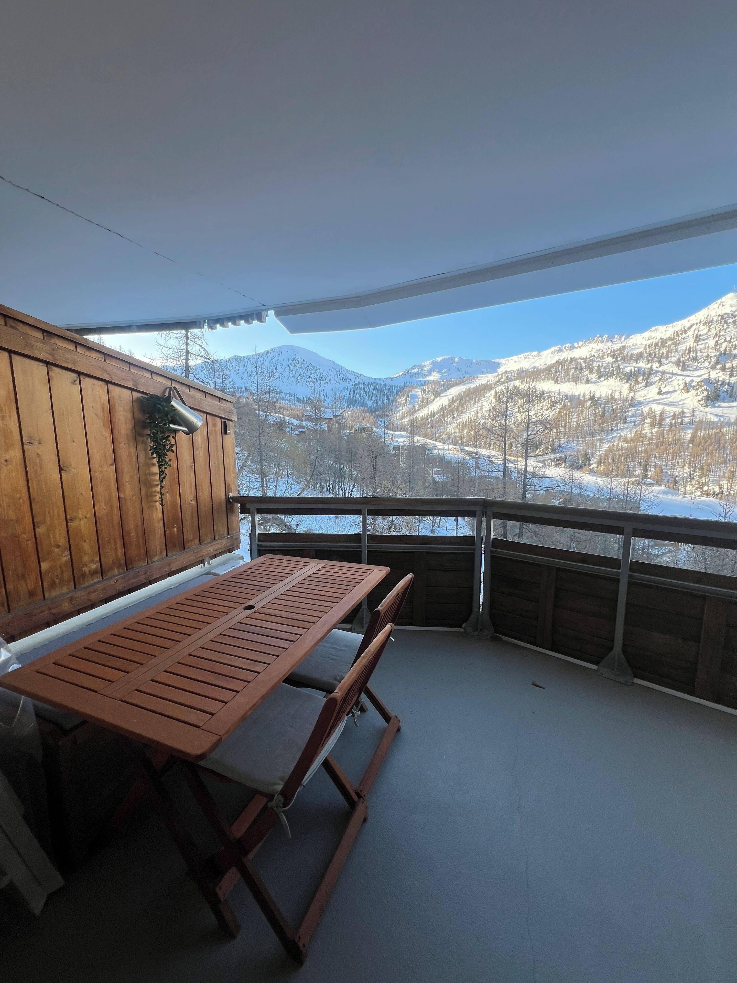 En træterrasse med et bord og stole, med udsigt over et sneklædt bjerglandskab.