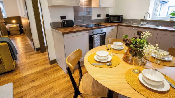 A compact kitchen with modern appliances, a dining area with a round table, and a view of the outdoors. - Oakwood Apartment (Llanrwst)