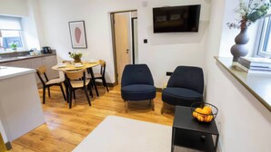A modern living room with a dining area, a TV mounted on the wall, and a window with a view. - Oakwood Apartment (Llanrwst)