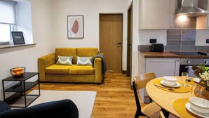 A compact living space with a sofa, a dining table set for two, a kitchen area with modern appliances, and a framed artwork on the wall. - Oakwood Apartment (Llanrwst)