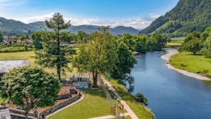 A riverside view with a pathway, trees, and a small building. - Oakwood Apartment (Llanrwst)