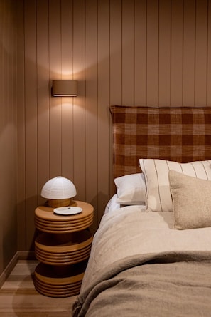A bedroom with a wooden headboard, a bedside lamp, and a stack of wooden stools. - Argyle North Boutique Yardley (North Hobart)