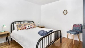 Quarto com uma cama, duas mesas de cabeceira, uma cadeira e um espelho fixado na parede.
