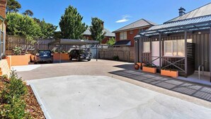 Uma entrada residencial com dois carros estacionados, uma garagem coberta e uma casa com telhado de metal e um pequeno jardim.