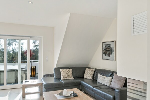 A modern living room with a sectional sofa, a coffee table, and a large sliding glass door leading to an outdoor area.