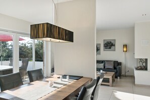 Ein modernes Wohnzimmer mit Essbereich, mit einem Holztisch, Stühlen, einer Couch und einer Pendelleuchte.