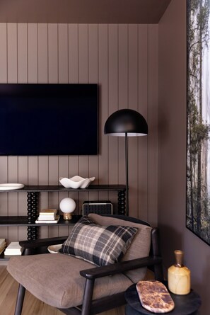 Een moderne woonkamer met een flatscreen televisie aan de muur, een vloerlamp, een bank met een ruitkussen, en een bijzettafeltje met een kaars.