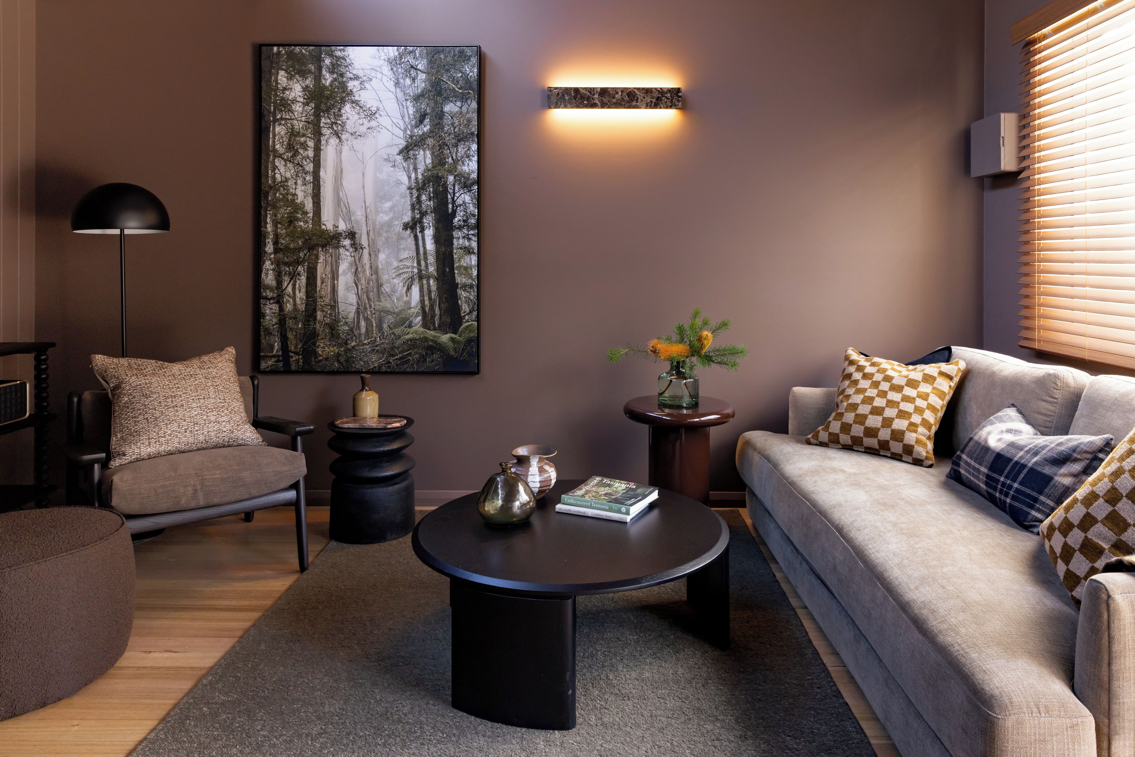 Ein modernes Wohnzimmer mit einer Couch, einem Sessel, einem Couchtisch und einem großen Wandbild mit Waldmotiv.