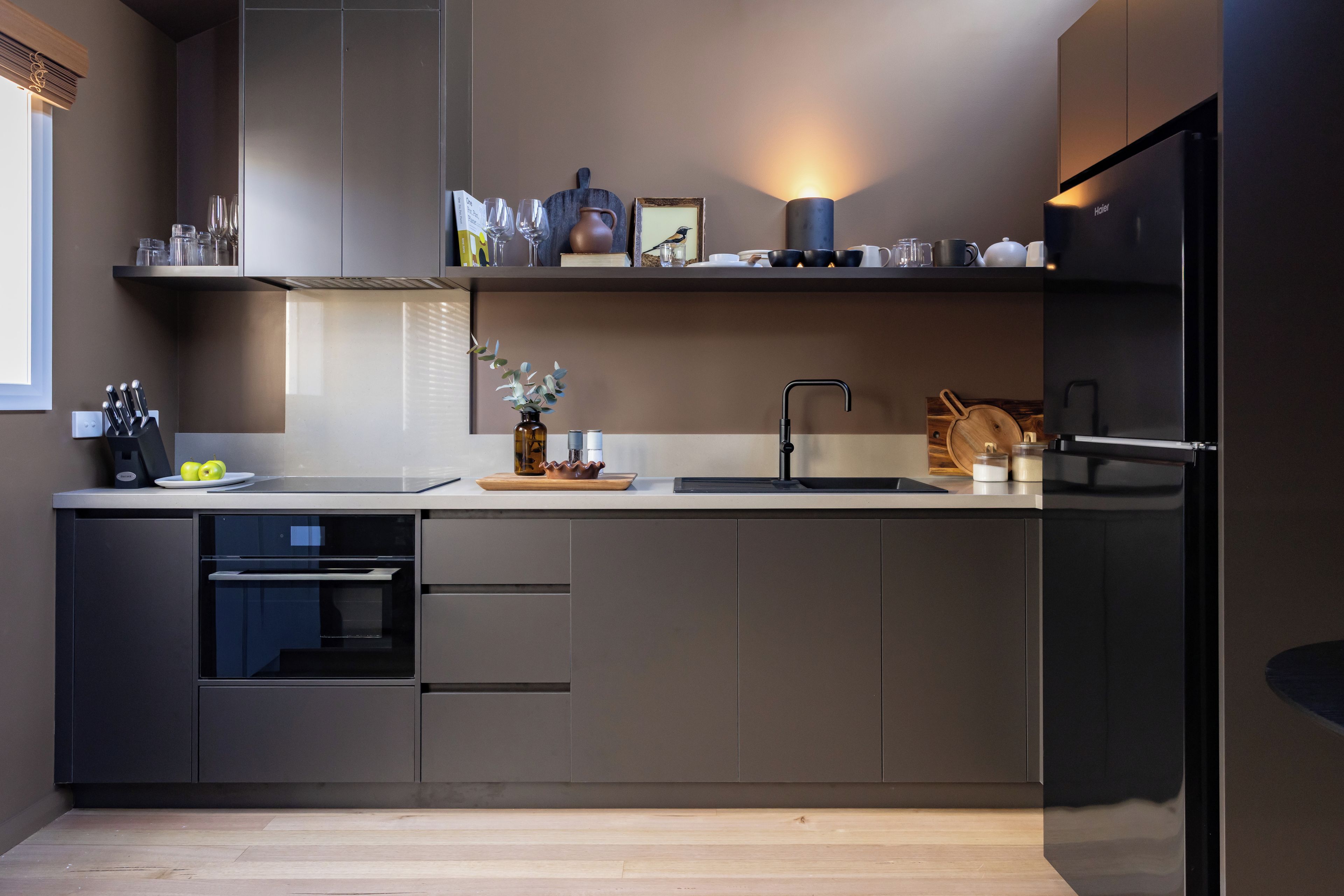 A modern kitchen with a built-in dishwasher, a black refrigerator, and a wooden countertop.