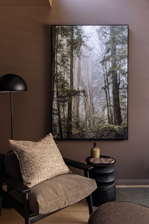 Une pièce comprenant un fauteuil moderne, une petite table d’appoint ronde et une grande œuvre d’art sur le thème de la forêt accrochée au mur.
