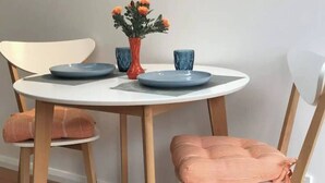Un comedor con una mesa redonda blanca, dos sillas con cojines a rayas, un jarrón con flores y dos tazas azules.