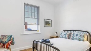 Une chambre à coucher avec un lit, une chaise, une fenêtre et une table de chevet.
