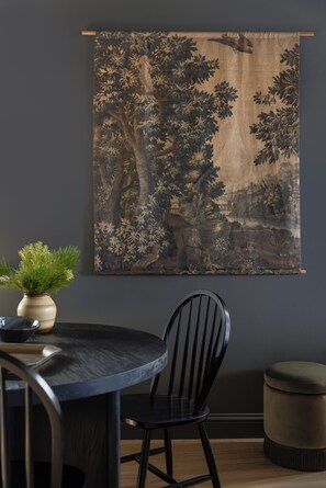Un coin repas avec une table ronde, une chaise noire, une plante en pot et une grande œuvre d’art encadrée au mur.