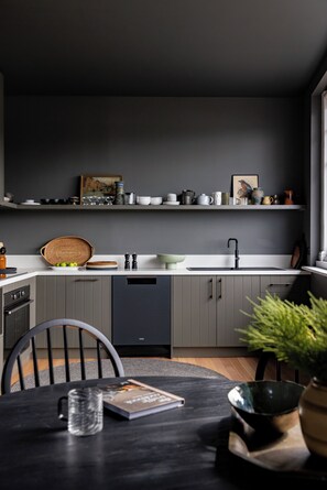 Une cuisine moderne avec des meubles gris, un lave-vaisselle noir et un plan de travail blanc.