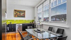 Une cuisine moderne avec une table à manger en verre, des chaises noires et un revêtement mural vert.