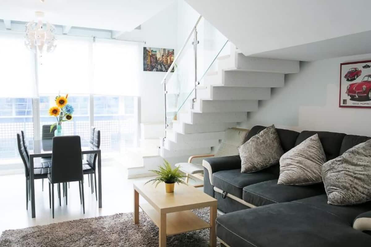 A modern living room with a black sofa, a coffee table, and a dining area with chairs and a vase of flowers.