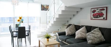 A modern living room with a black sofa, a coffee table, and a dining area with chairs and a vase of flowers.